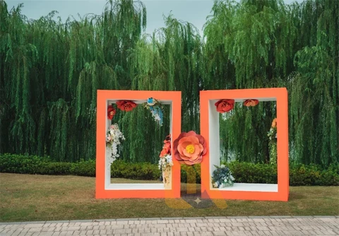 Two orange photo frames with flower decorations in front of willow trees.