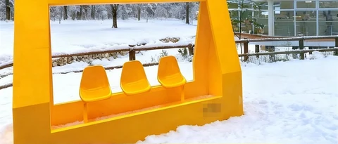 A close view of three suspended seats inside a yellow frame in the snow.