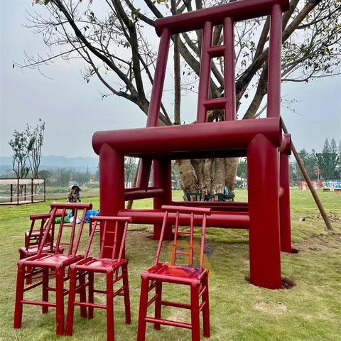 An oversized red chair displayed with smaller chairs on a lawn.
